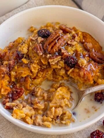 A white bowl filled with pumpkin oatmeal, pecans, and dried cranberries.