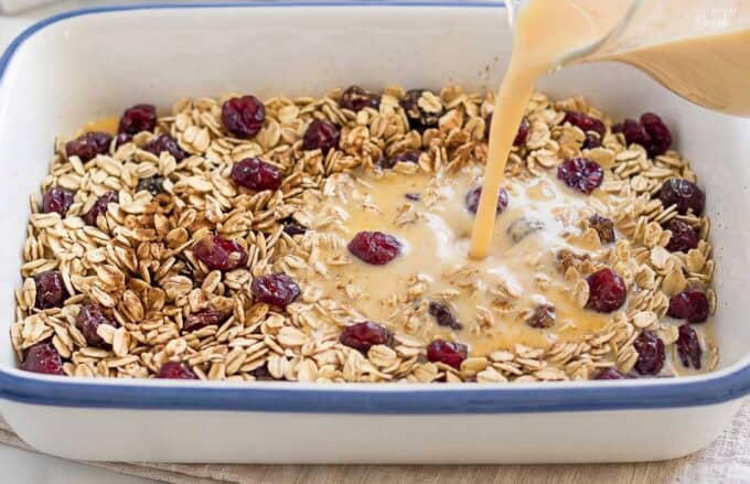 Pumpkin custard being poured over oats in a blue and white baking dish.