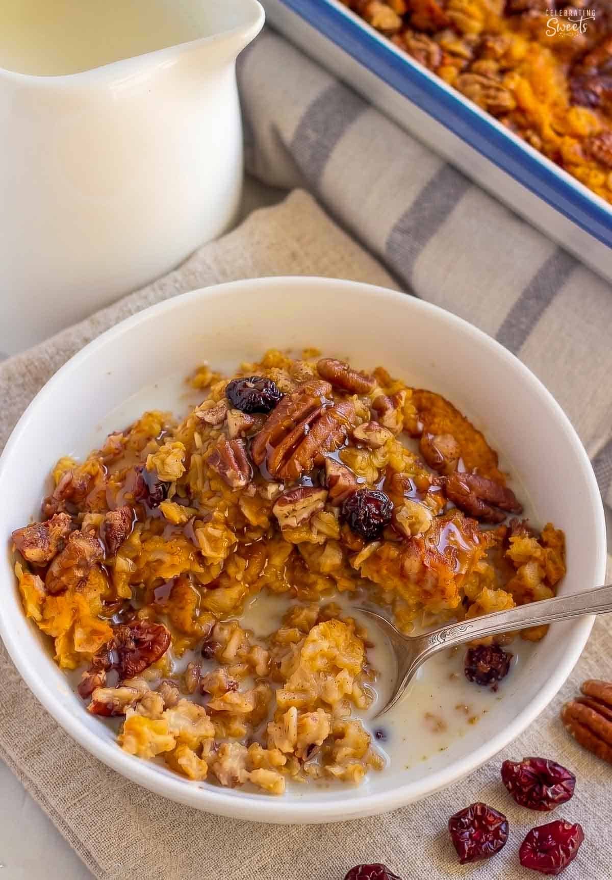 A white bowl filled with pumpkin oatmeal, pecans, and dried cranberries.