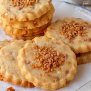 Shortbread cookies topped with toffee bits sitting on parchment paper.