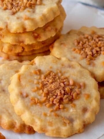Shortbread cookies topped with toffee bits sitting on parchment paper.