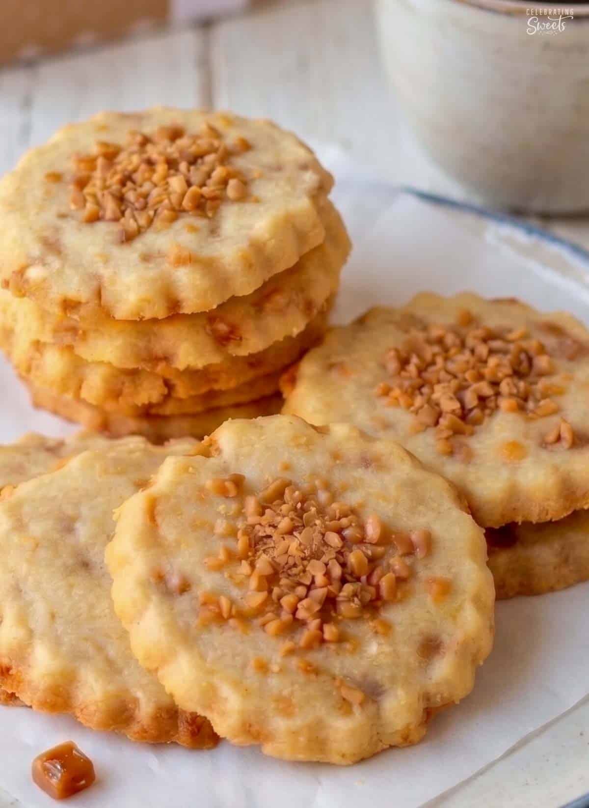 Shortbread cookies topped with toffee bits sitting on parchment paper.