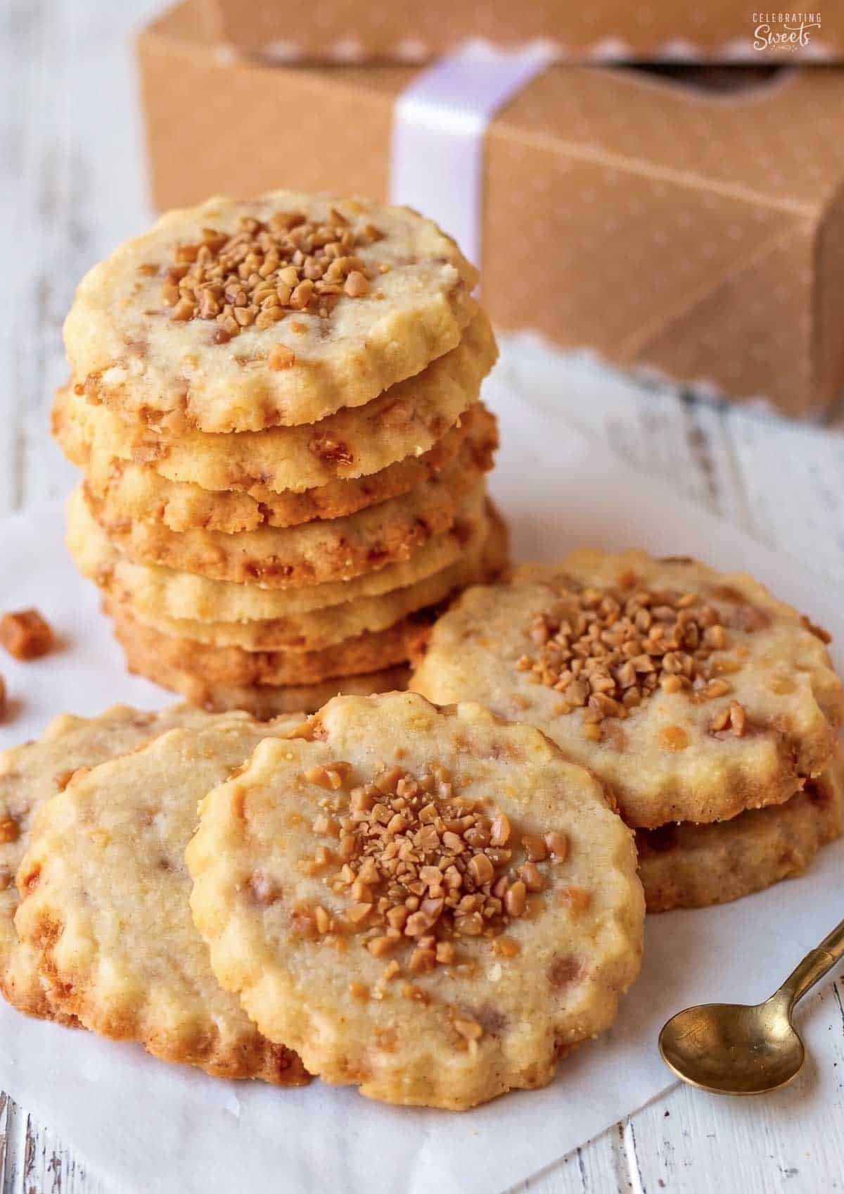 Stack of shortbread cookies topped with toffee bits with small boxes in the background.