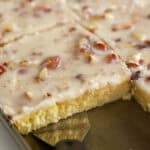 White Texas sheet cake topped with almonds in a baking pan with a metal spatula.