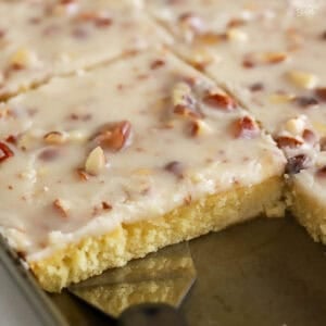 White Texas sheet cake topped with almonds in a baking pan with a metal spatula.