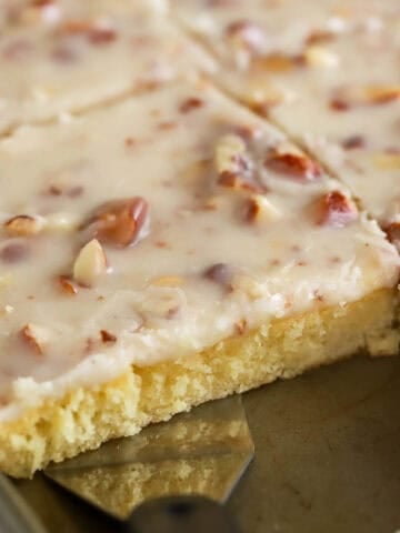 White Texas sheet cake topped with almonds in a baking pan with a metal spatula.