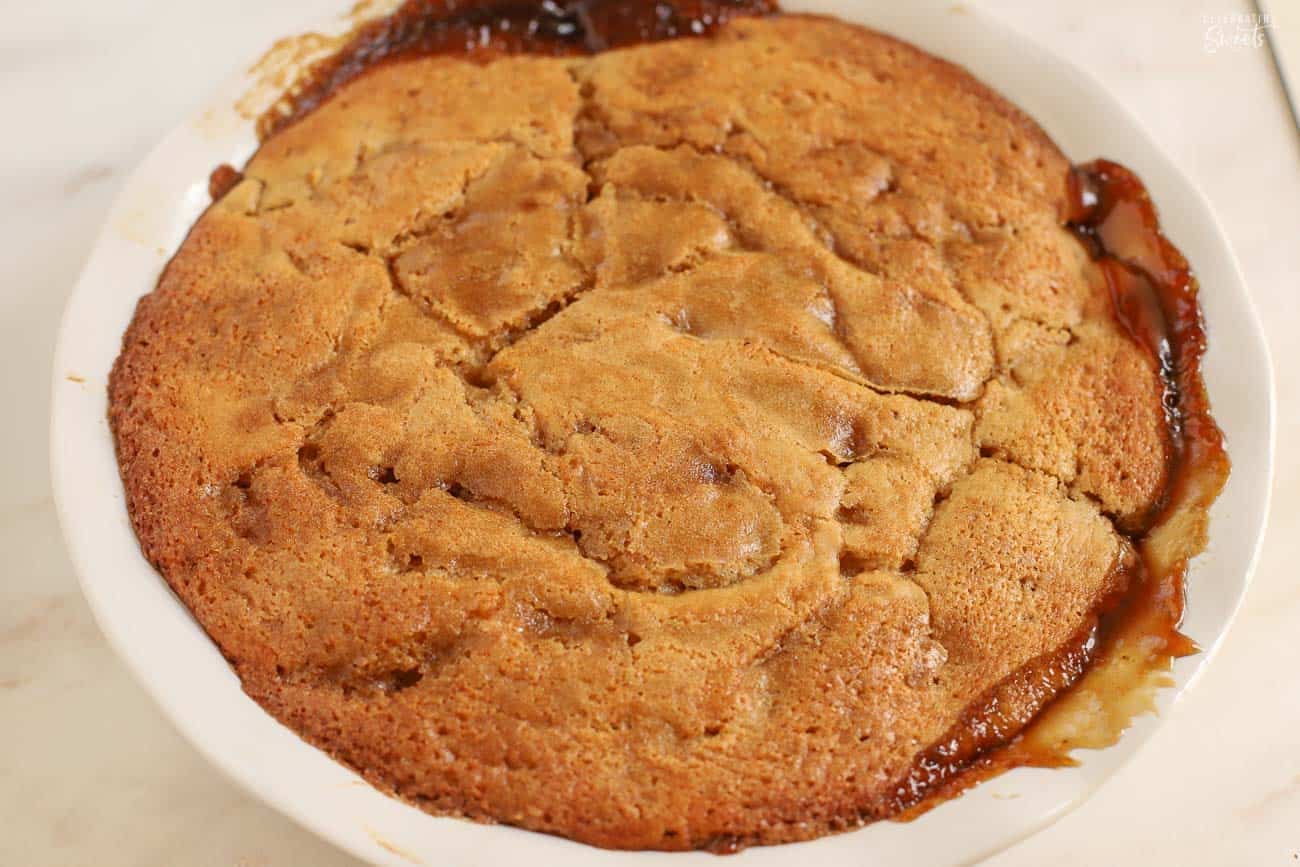 Caramel apple cake in a round cake pan on a marble board.