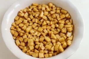 Diced apples tossed in cinnamon sugar in a white round baking dish.