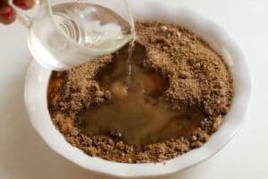 Water being poured over brown sugar and cake batter in a white baking dish.