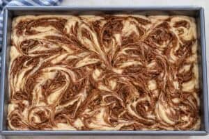 Cake batter with swirls of cinnamon butter in a metal pan.