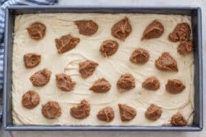 Cake batter topped with dollops of cinnamon butter in a cake pan.