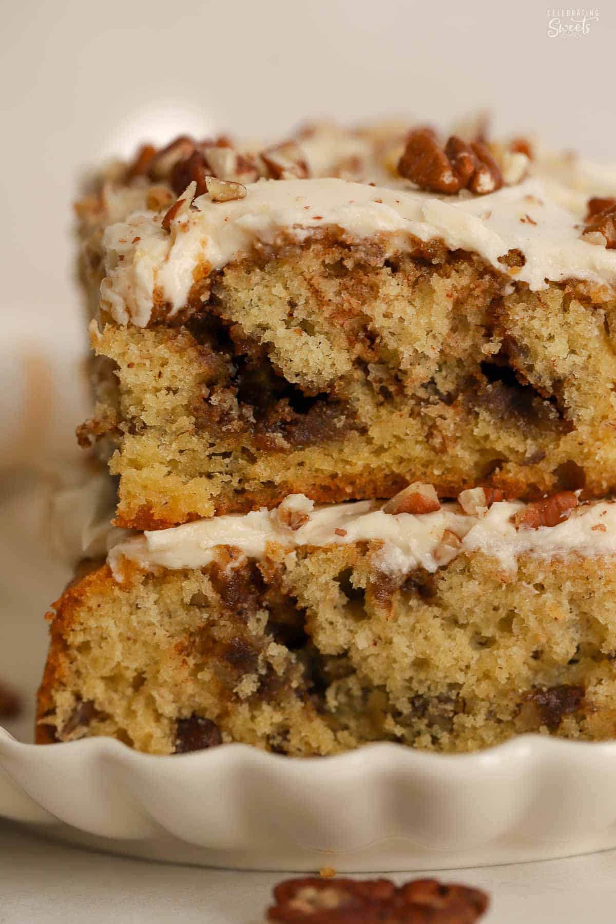 Two slices of maple coffee cake stacked on top of each other on a white scalloped plate.