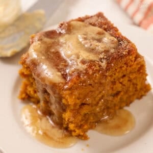 Square slice of pumpkin cake on a white plate topped with melted honey butter.