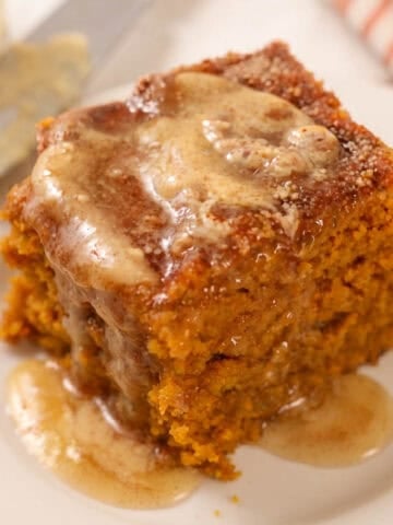 Square slice of pumpkin cake on a white plate topped with melted honey butter.