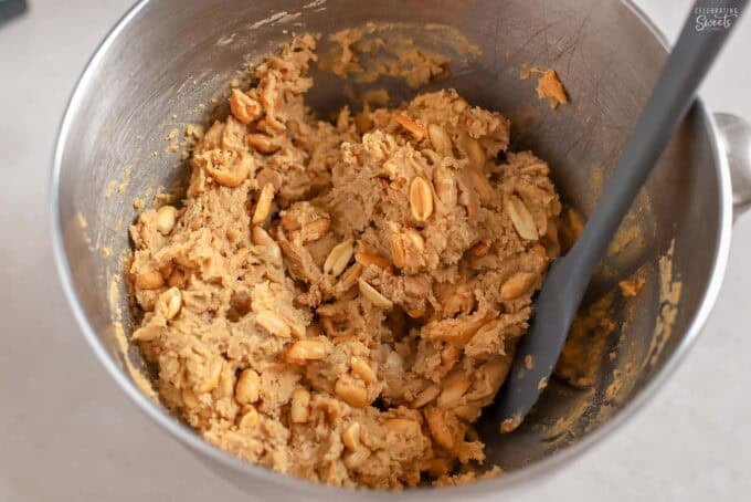 Peanut cookie dough in a mixing bowl next to a grey spatula.