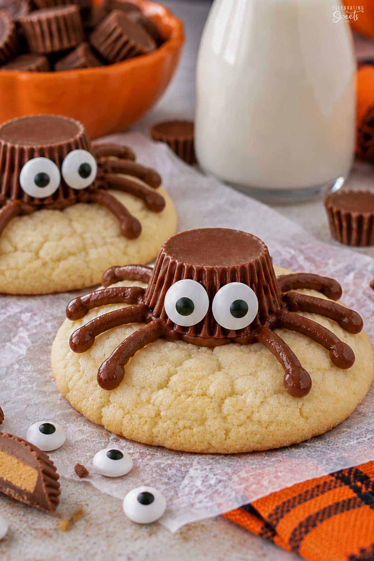 Spider cookies (made from sugar cookies, chocolate frosting, and peanut butter cups) on parchment paper next to an orange napkin.